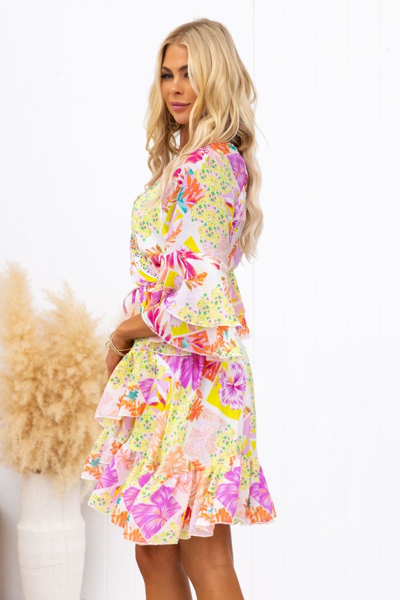 Side view of a woman in a colorful floral Fools Gold Wrap Dress with ruffles and a V-neckline.