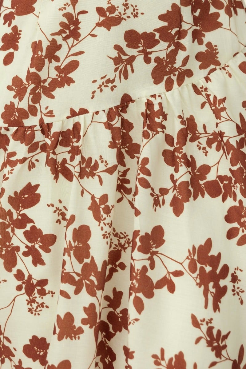 Close-up of floral print fabric in warm tones on Heartbreak Maxi Dress, showcasing intricate leaf and flower patterns.