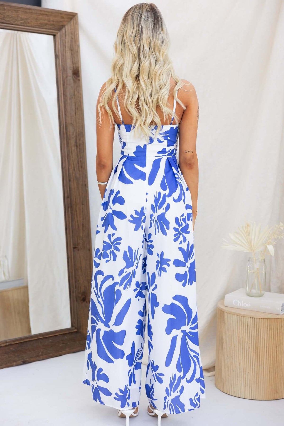 Model wearing a floral Ivy jumpsuit with adjustable straps and pockets, viewed from the back in a stylish setting.