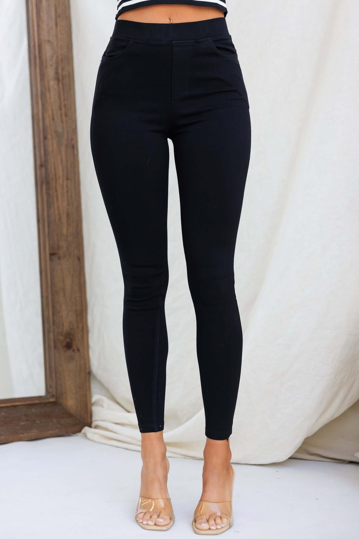 Black jeggings pants with mid-high waist, elastic waistband, and pockets displayed on a model.