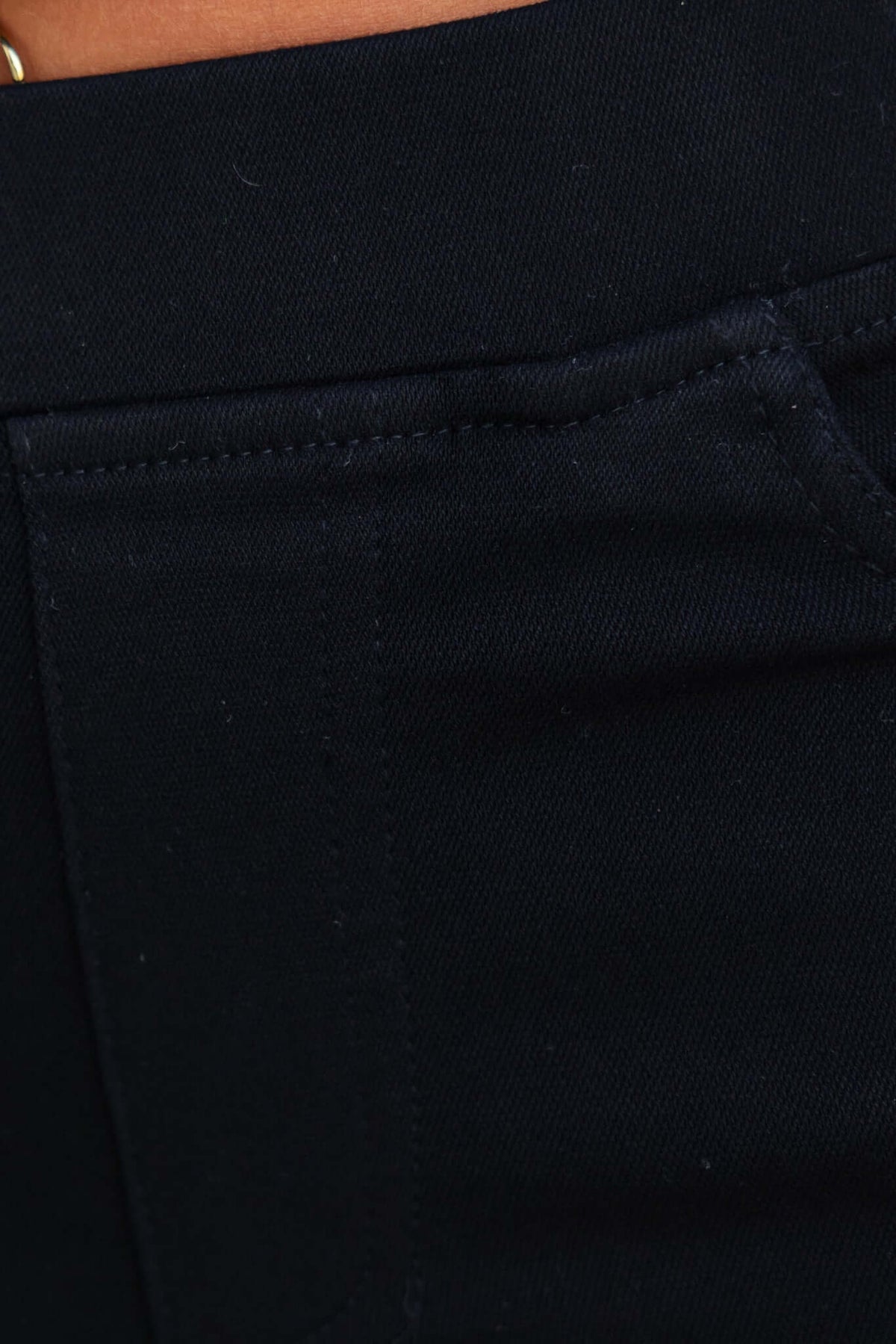 Close-up of black jeggings with a mid-high waist, featuring elastic waistband and pocket detail.