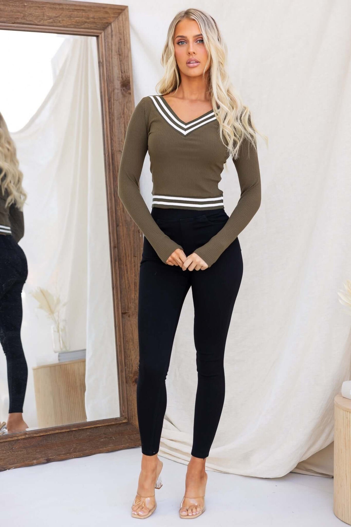 Model wearing olive green Harford Top with V-neckline and stripes, paired with black leggings in a stylish indoor setting.