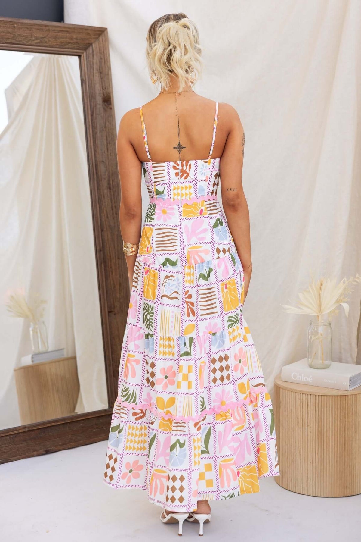 Back view of a woman in a colorful Miffy maxi dress with adjustable straps and a flared skirt, styled with shoes.