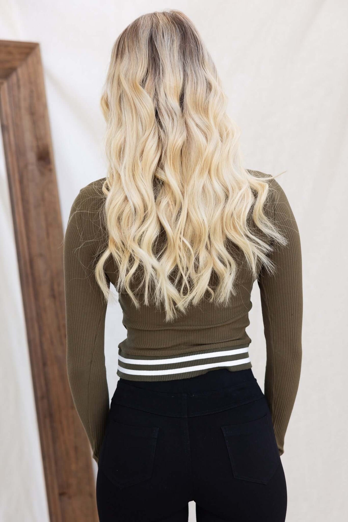 Back view of a woman wearing an olive green ribbed Harford Top with long wavy blonde hair and black high-waisted pants.
