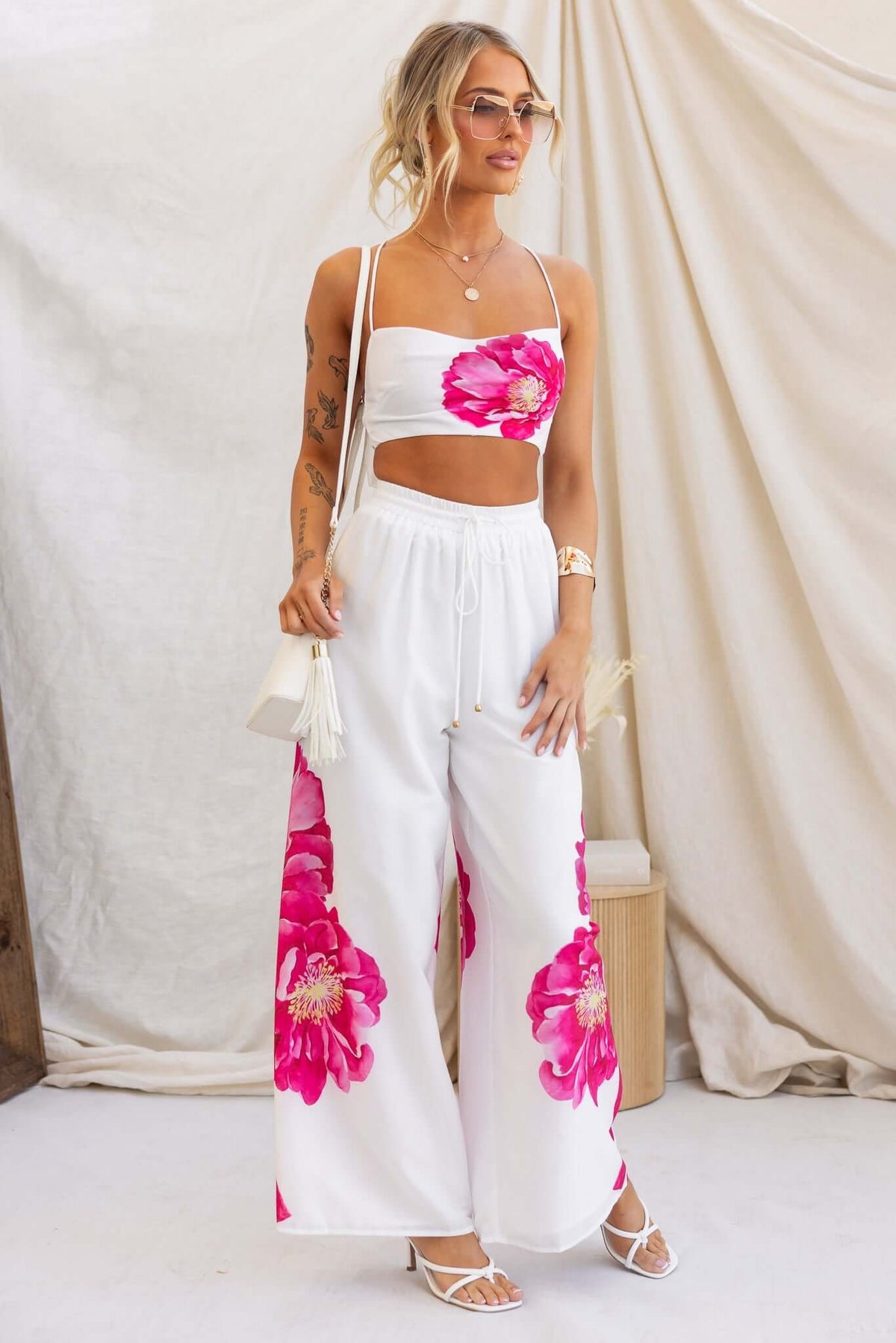 Model wearing the Faly Top with adjustable straps and floral print, paired with wide-leg pants in a bright, summer setting.