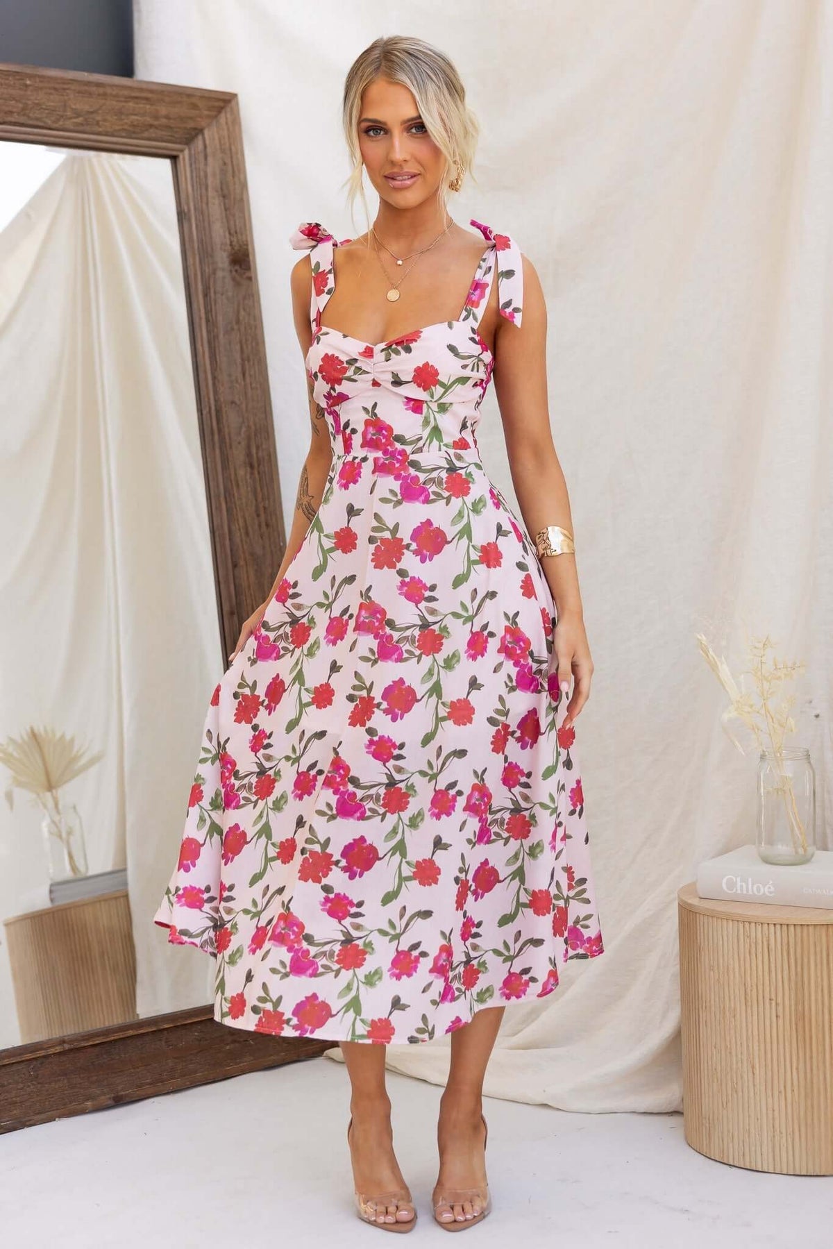 Floral print midi dress with adjustable tie straps and an invisible zip at back, worn by a model in a stylish setting.