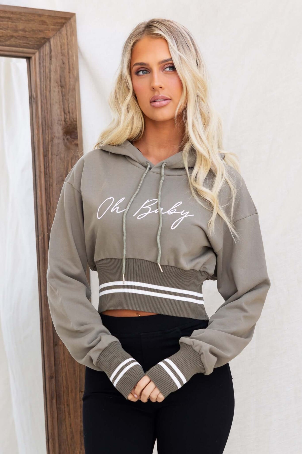 Stylish cropped olive green jumper hoodie with drawstring, featuring a trendy "Oh Baby" design and striped cuffs.