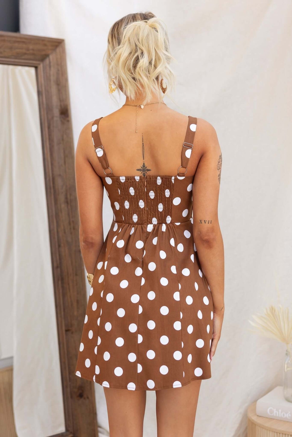 Brown polka dot Isibel dress with adjustable straps, smocked back, and pockets, displayed on a model from the back.