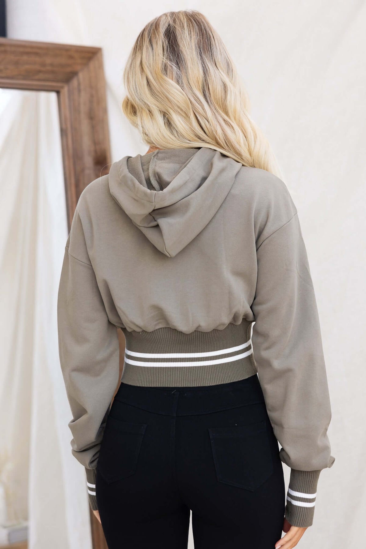Back view of Ross Jumper in olive green with a drawstring hood and elastic hem, styled with black pants.