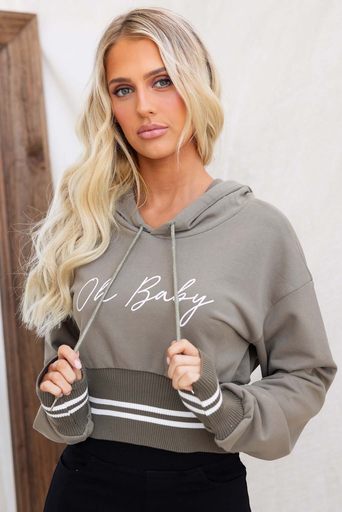 Model wearing a stylish olive green Ross Jumper hoodie with 'Old Baby' print and drawstring, perfect for casual outfits.