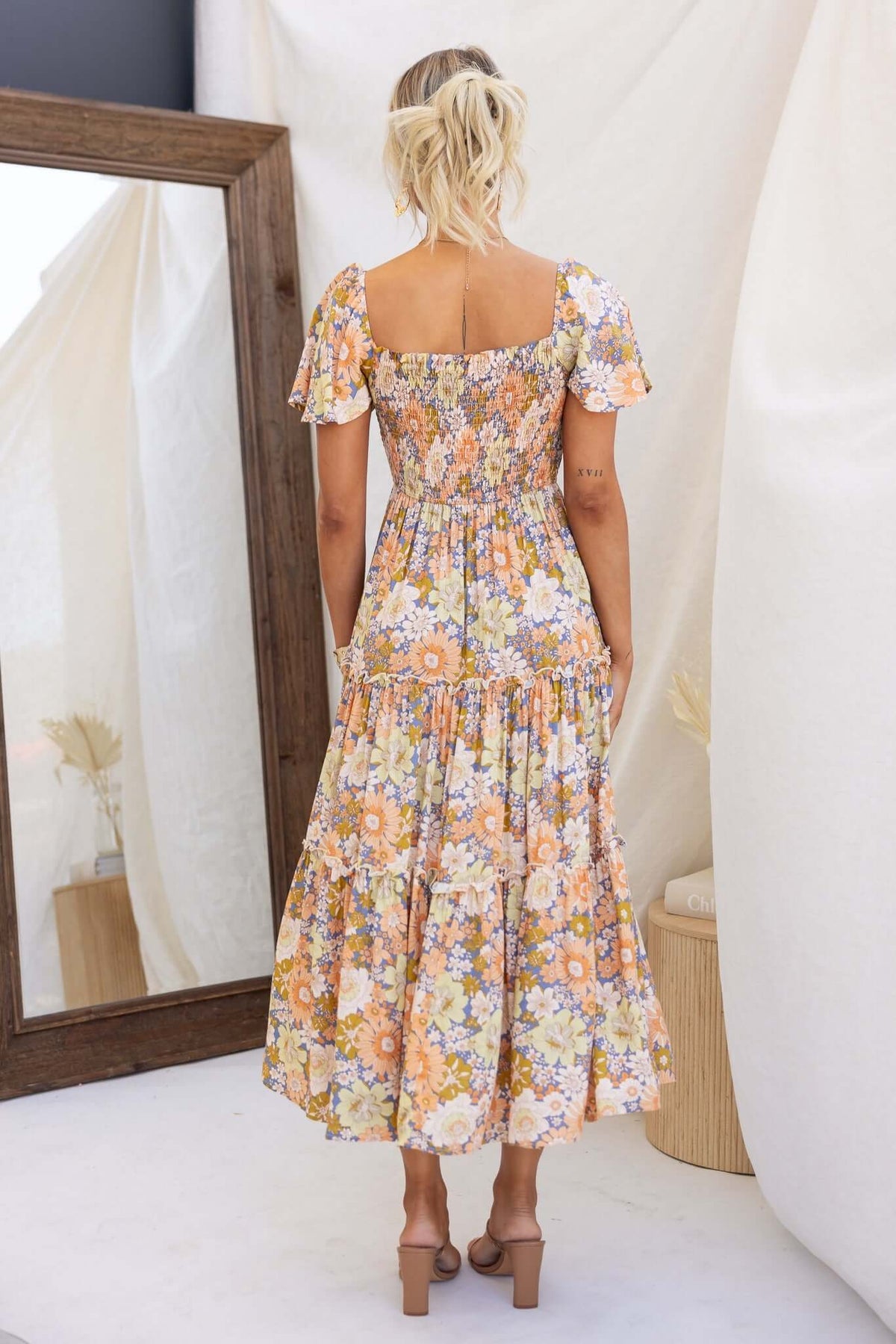 Back view of a floral maxi dress with short sleeves, featuring an elastic bodice and pockets, perfect for a nostalgic look.
