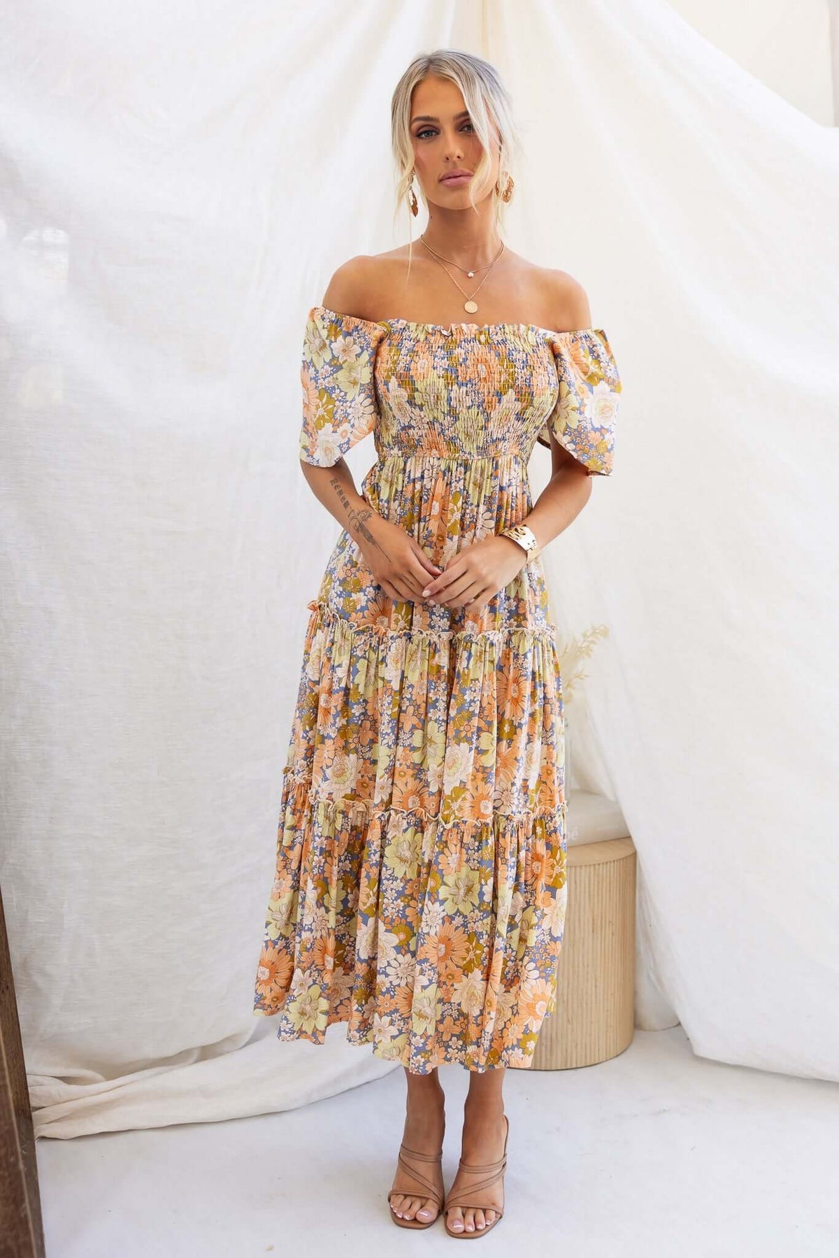 Model wearing a nostalgic maxi dress with an elastic bodice, off-shoulder sleeves, and floral print, styled with heeled sandals.