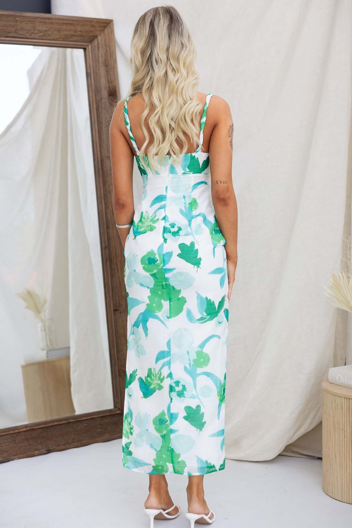 Woman wearing a floral green Riverside Maxi Dress, showing the back design with twist straps and split at the side.