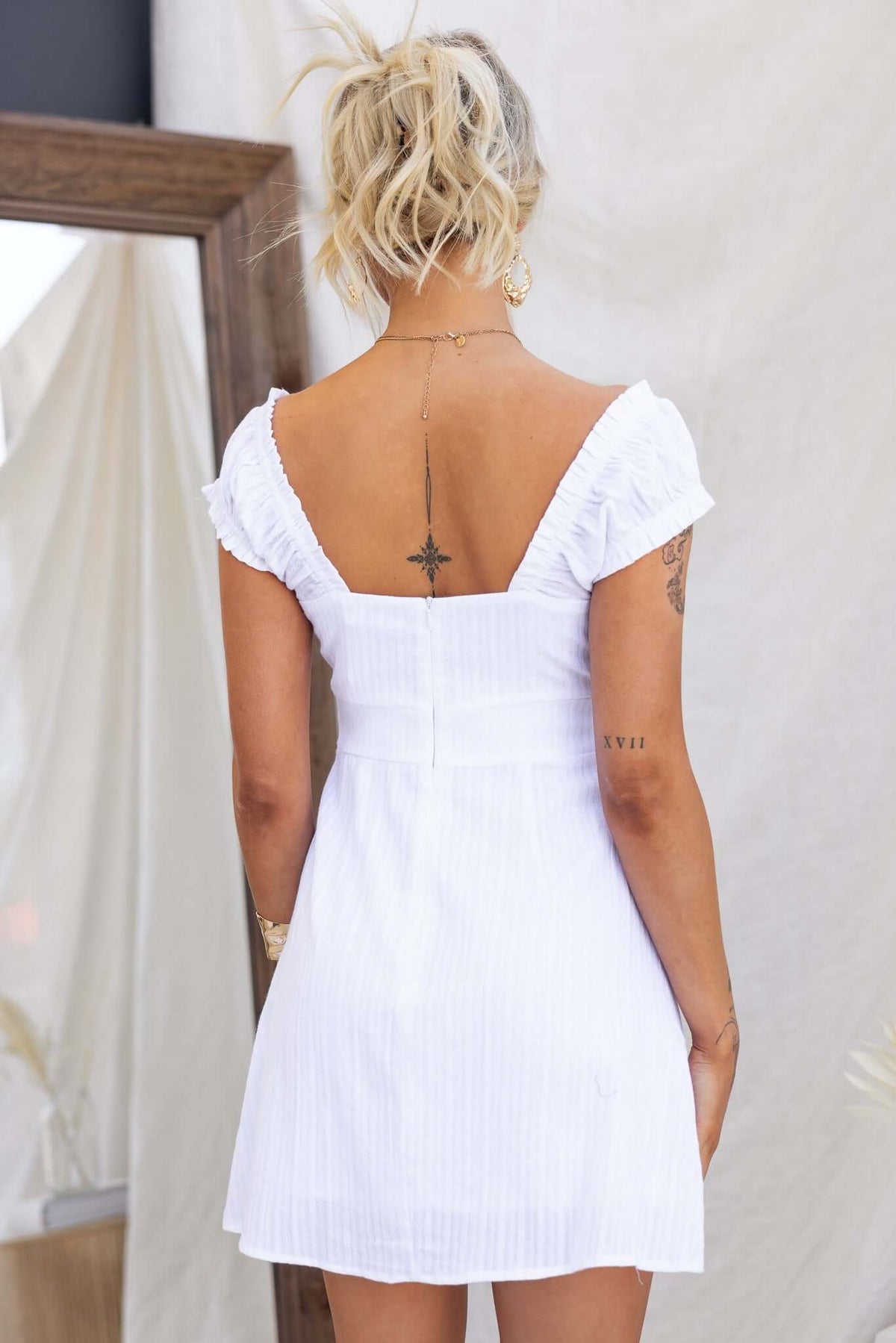 Back view of the Calyssa Dress featuring elastic sleeves and a button-up bust in a stylish white fabric.