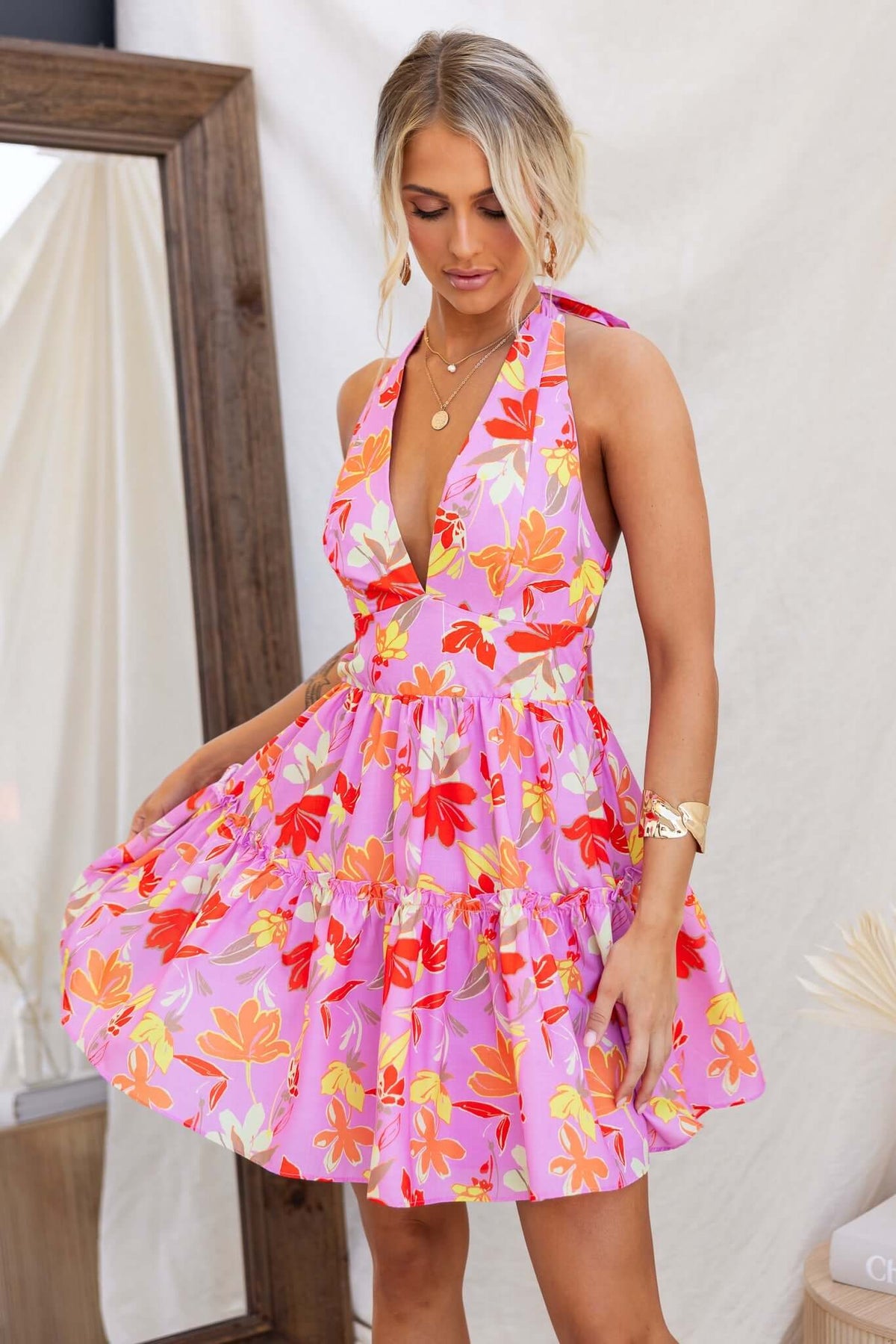 Model wearing a pink Buttercup Dress with floral patterns, featuring a tie neckline and flared skirt.