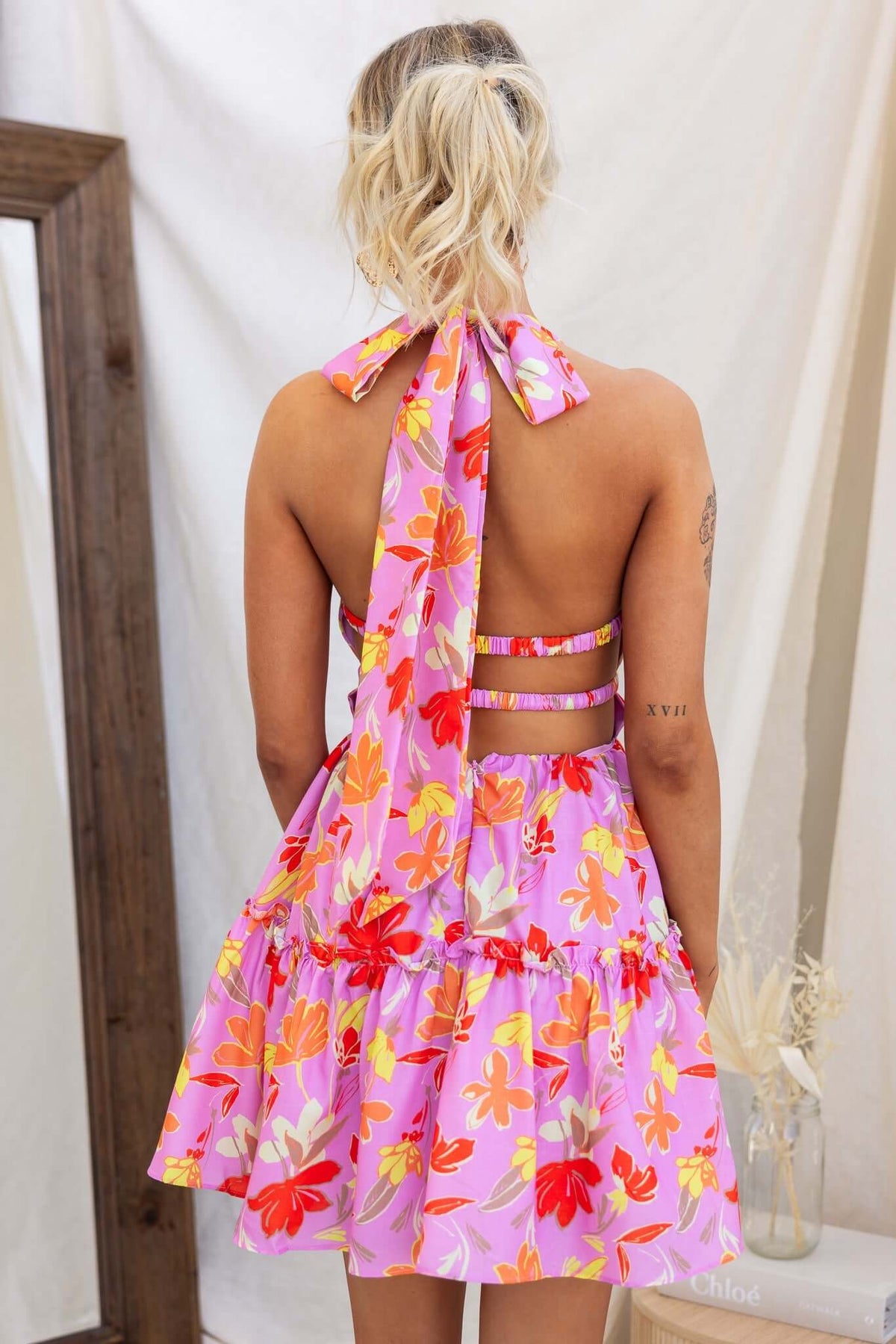 Back view of the Buttercup Dress featuring a floral design, tie neckline, and layered skirt.