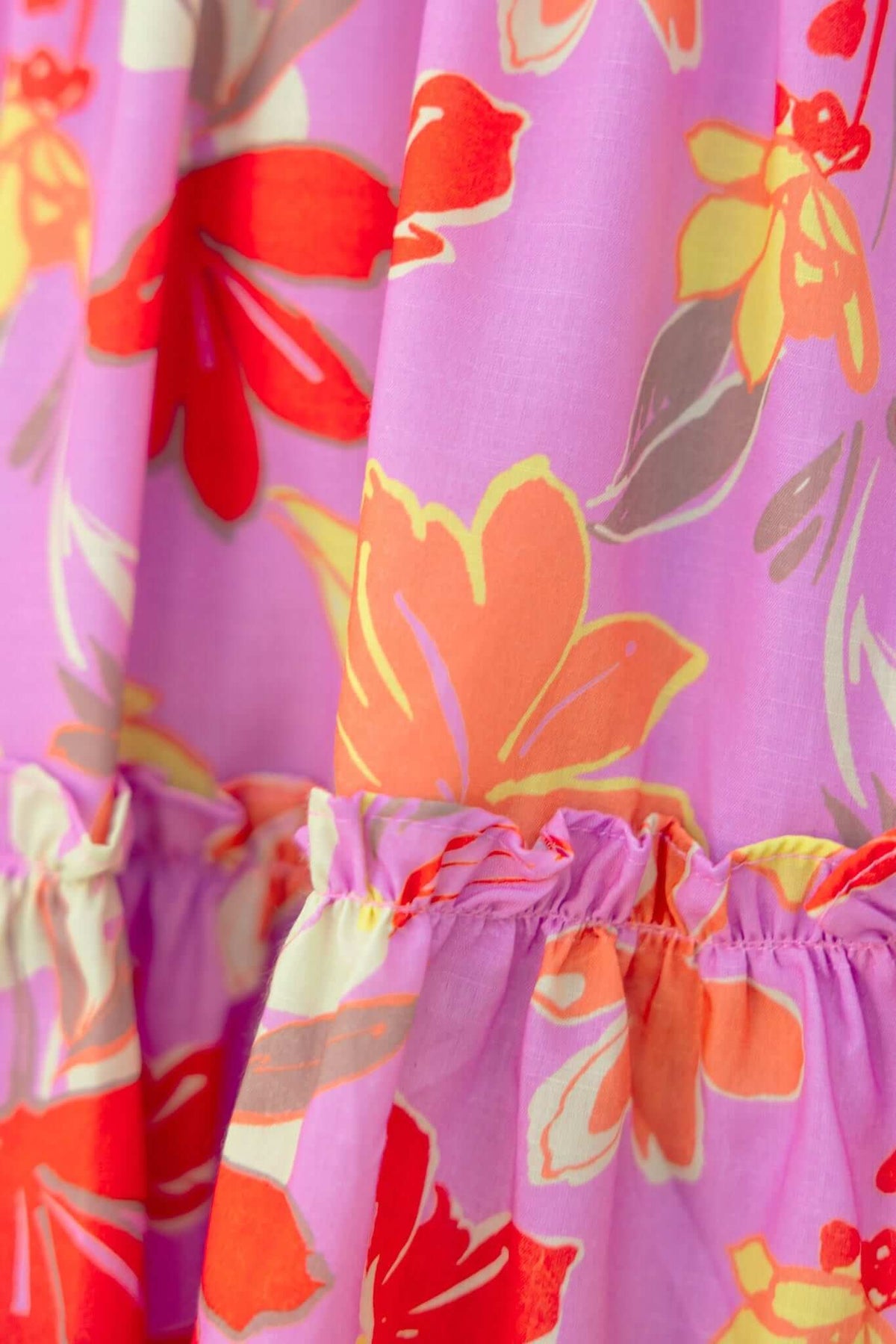Close-up of Buttercup Dress featuring vibrant floral patterns in pink and orange, showcasing tie neckline and ruffled hem.