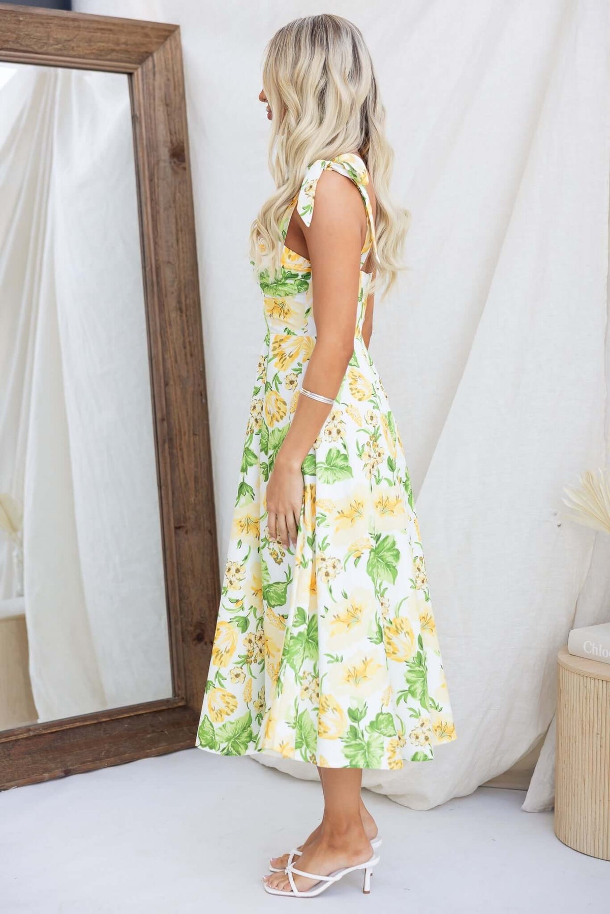 Floral print midi dress with adjustable tie straps, styled on a model in a natural setting with a mirror.
