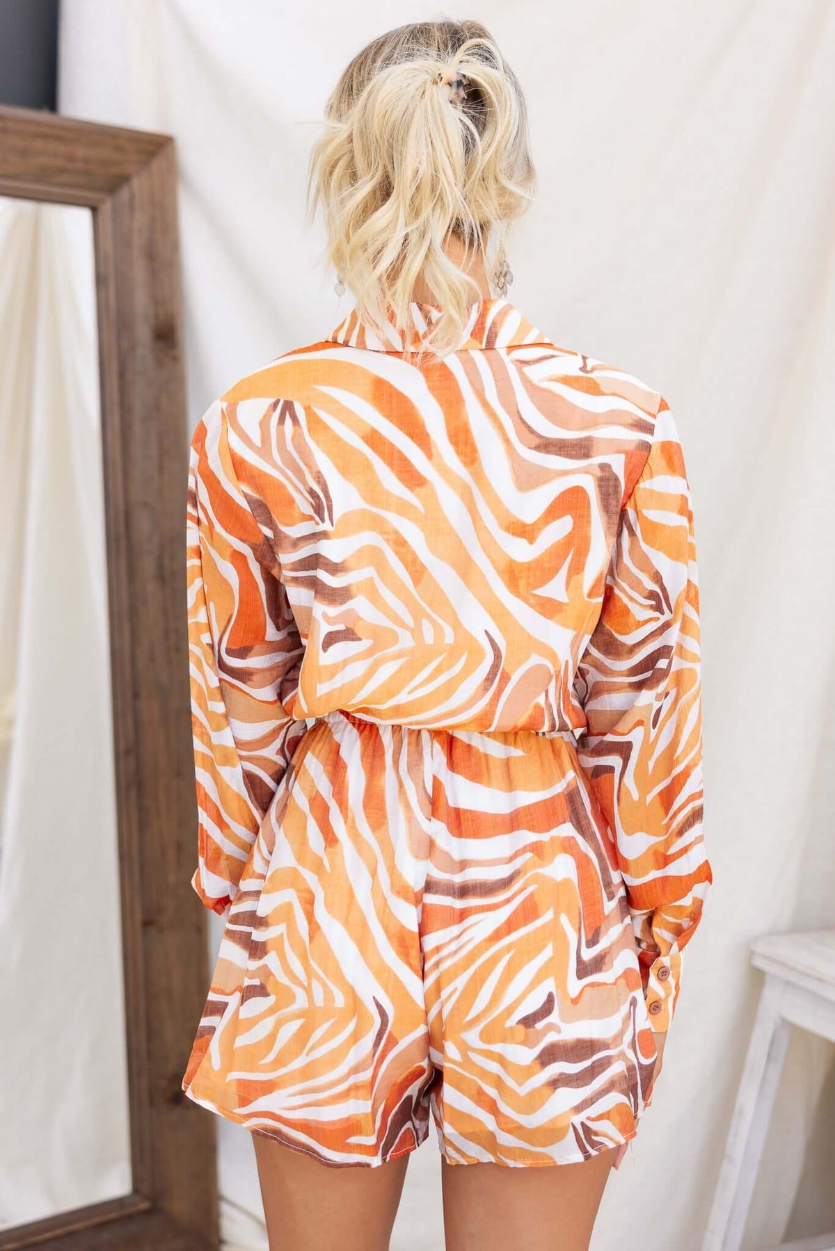 Back view of a woman wearing an orange and cream striped Oregon playsuit with a collar and elastic waistband.