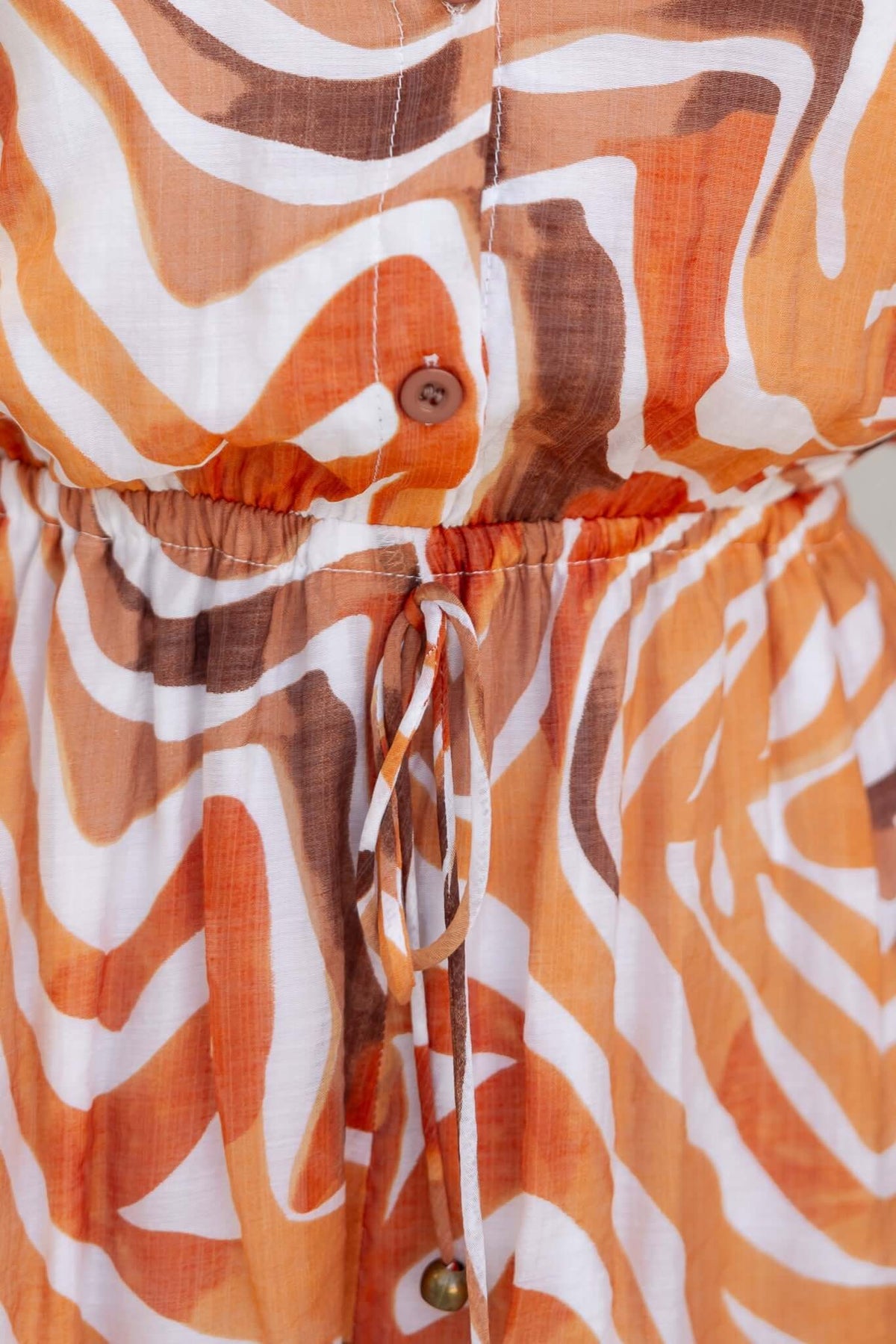 Close-up of Oregon Playsuit featuring an elastic waistband, tie detail, and abstract orange and brown pattern.