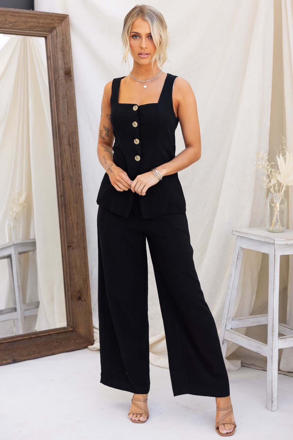 Model wearing a black vest style top with button-up front and wide-leg pants, showcasing a chic and stylish outfit.