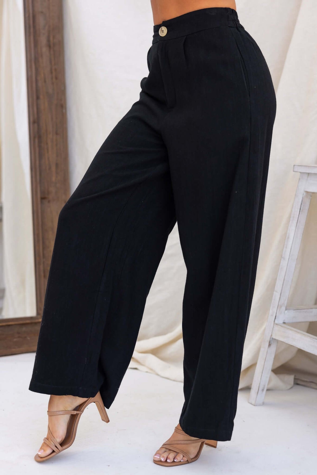 Bexley Pants in black, featuring a mid-high waist, elastic waistband, pockets, and a linen look, styled with heels.