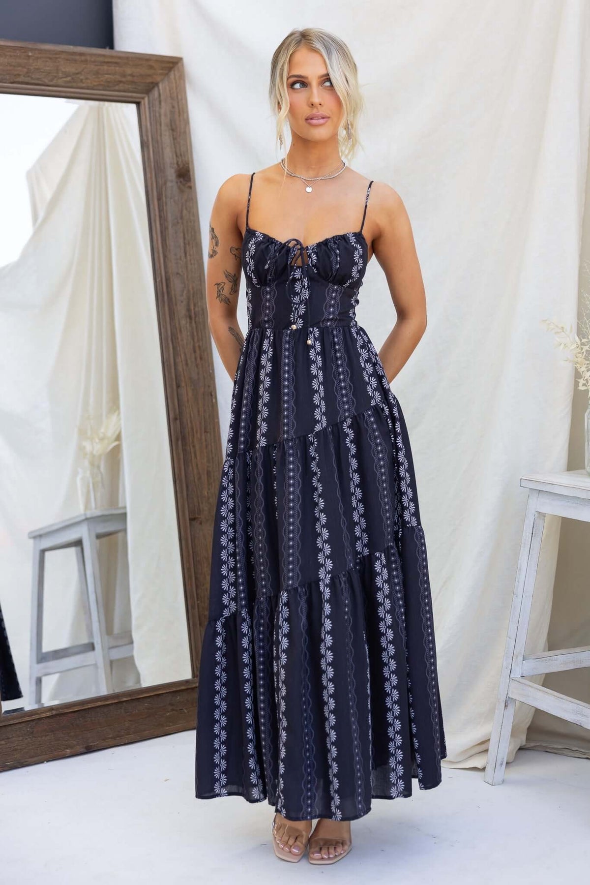 Model wearing a black Eider Maxi Dress with adjustable straps and a tie at the bust, featuring a layered design.