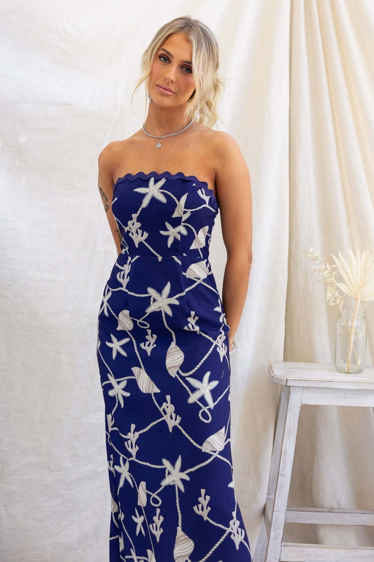 Model wearing a navy strapless Safran maxi dress with floral design, featuring a scalloped top and elegant fit.