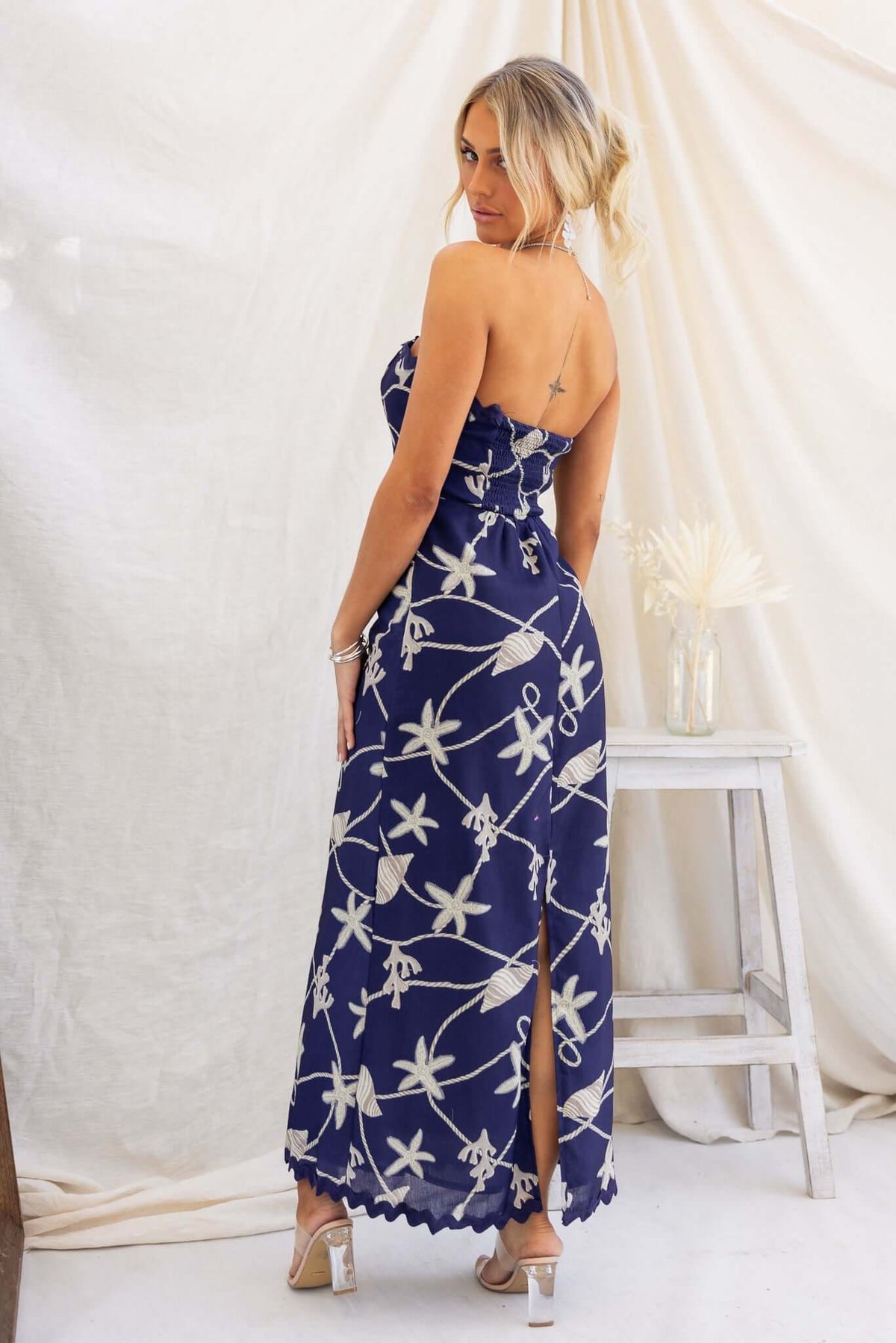 Model wearing a navy strapless maxi dress with a floral design, showing a side split and back view.