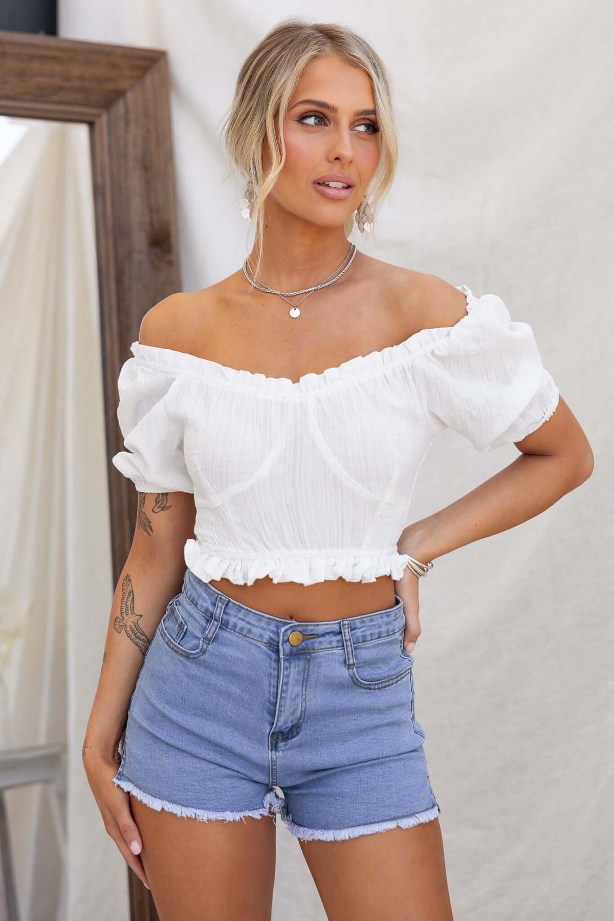 Model wearing off-shoulder Fresno Top in white with denim shorts, showcasing cotton blend fabric and relaxed fit.