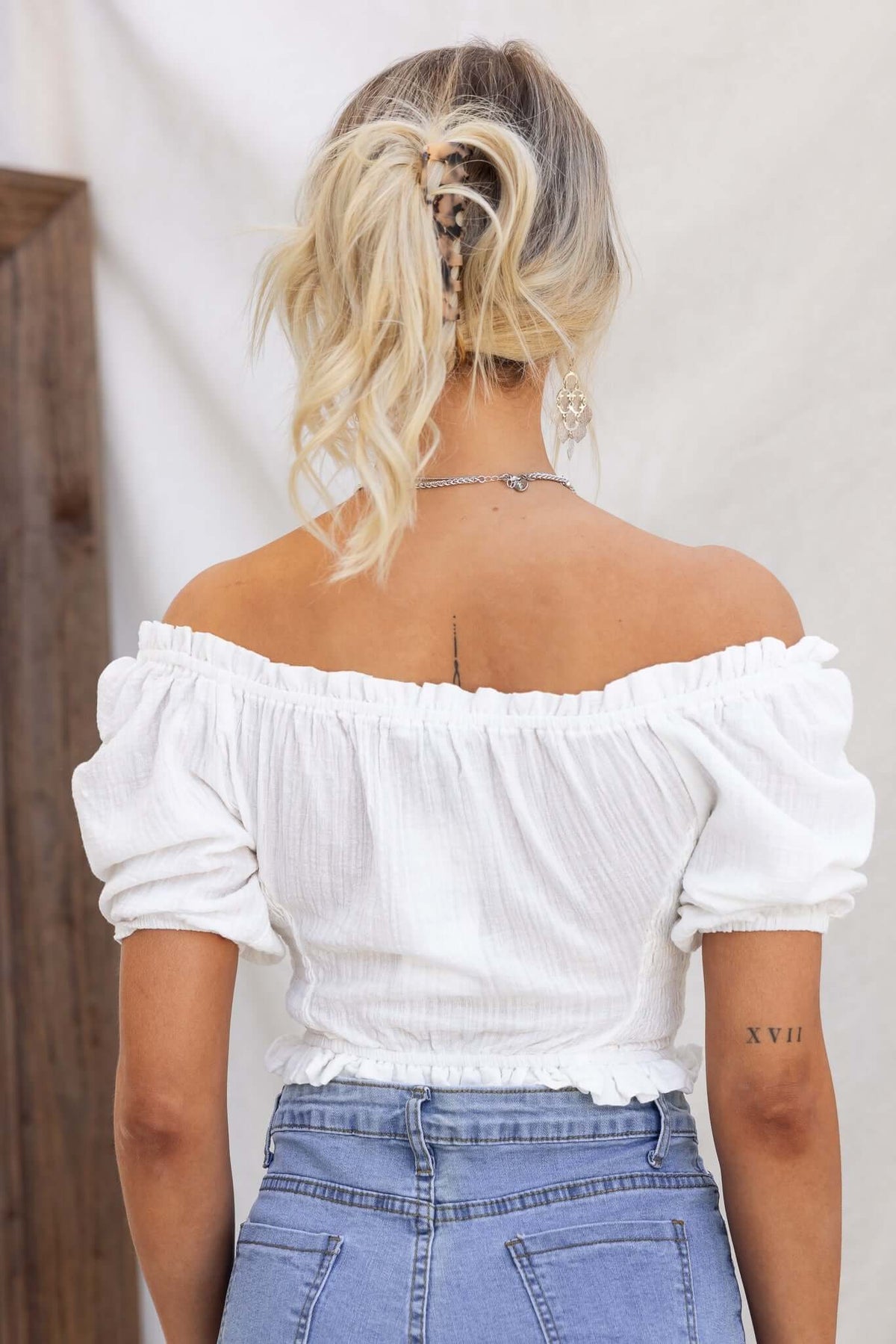 Back view of a woman wearing a white off-shoulder Fresno Top with puffy sleeves, paired with denim jeans.