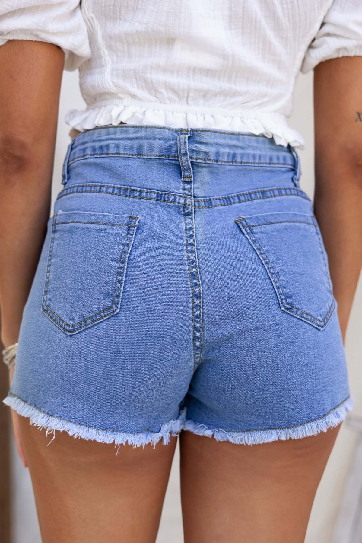 Back view of Too Cool Denim Shorts featuring high-mid waist, frayed hem, and pockets.