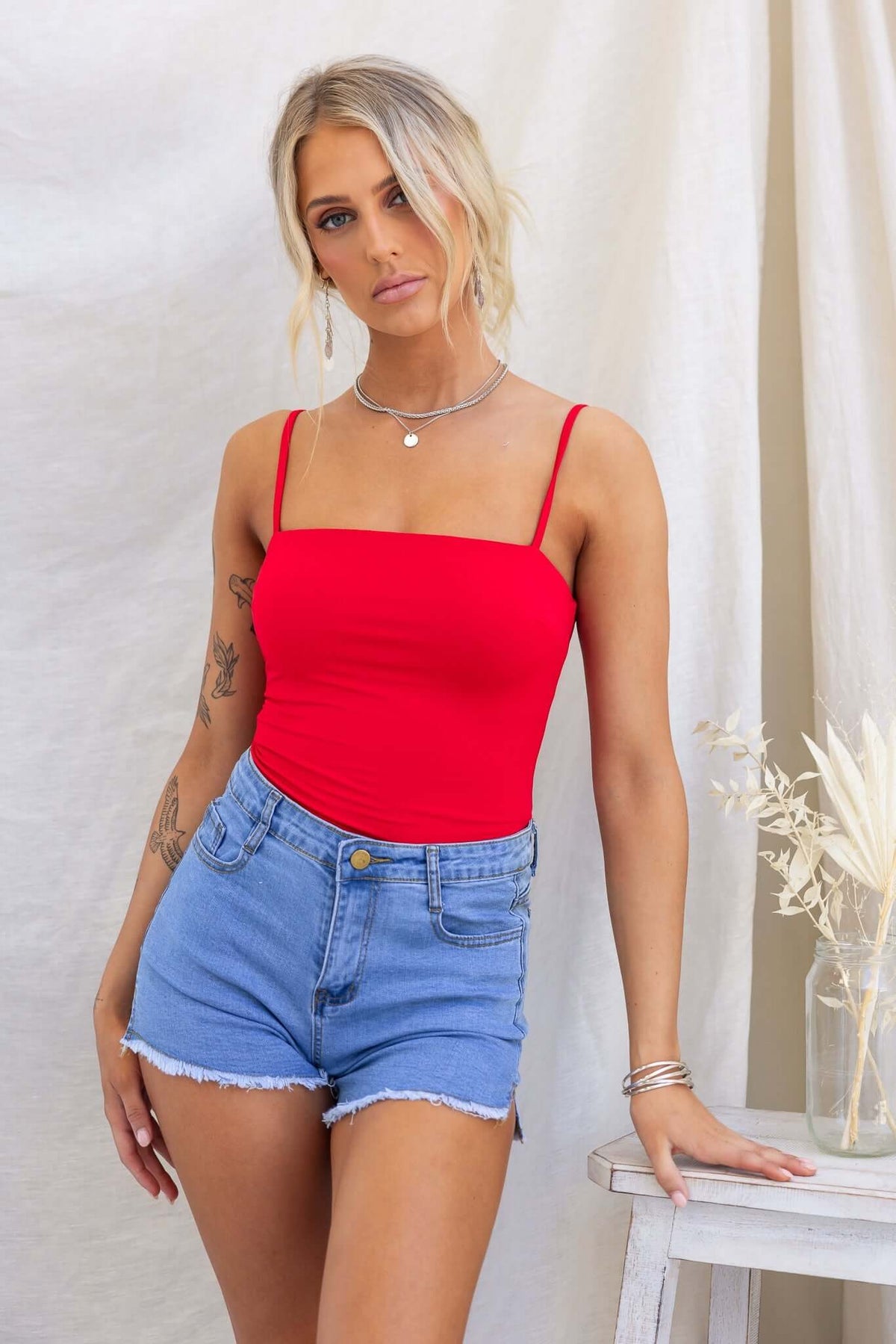 Brea Bodysuit in red with adjustable straps and square neckline, paired with denim shorts for a stylish look.