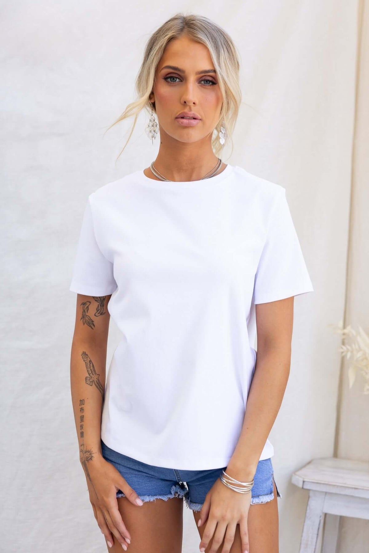 Woman wearing a white Doha Tee with round neckline and short sleeves, styled with denim shorts.