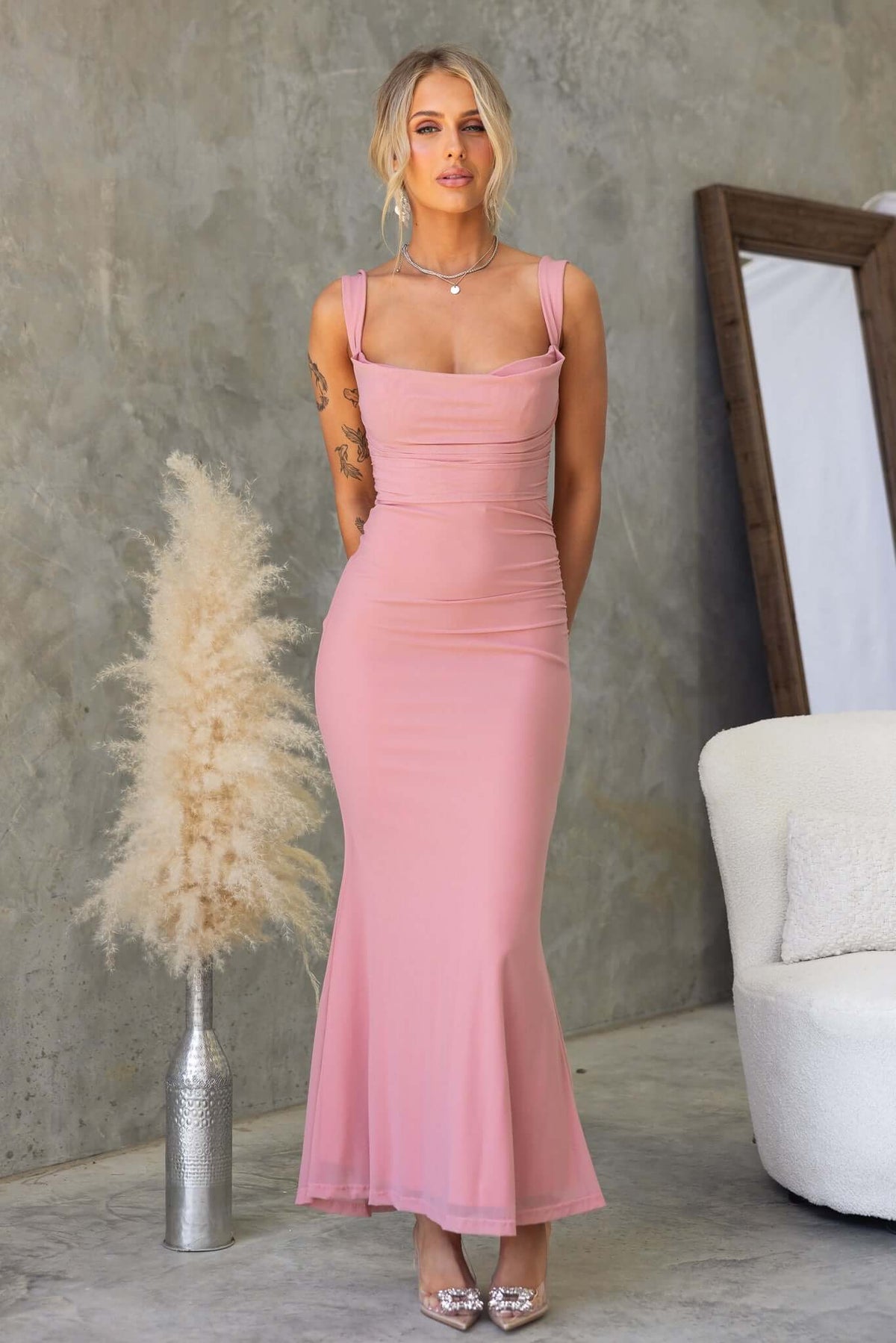 Model wearing Inaya Maxi Dress in pink with adjustable straps against a textured background.