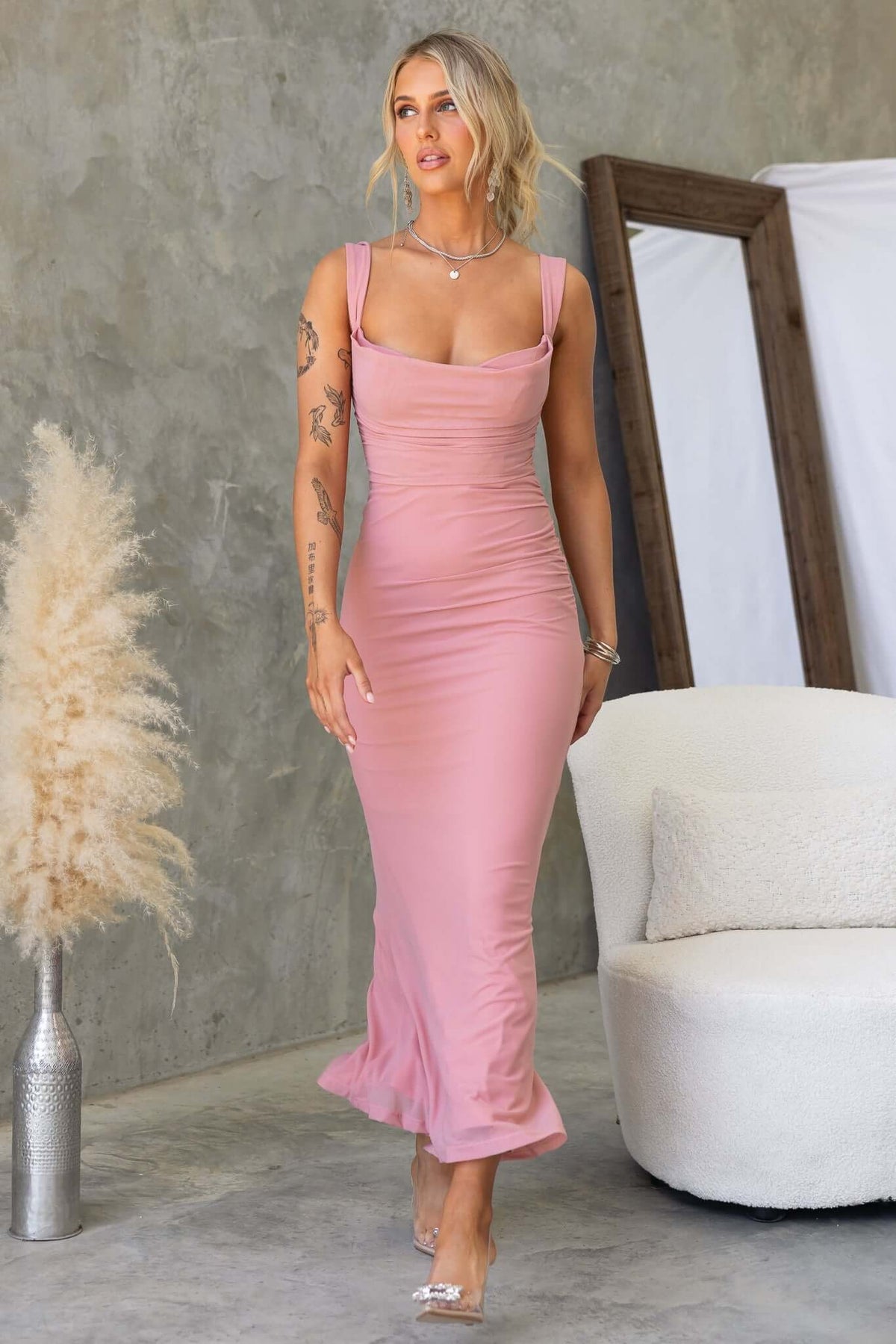 Inaya Maxi Dress in blush pink, featuring adjustable straps and a fitted silhouette, styled in a modern setting.