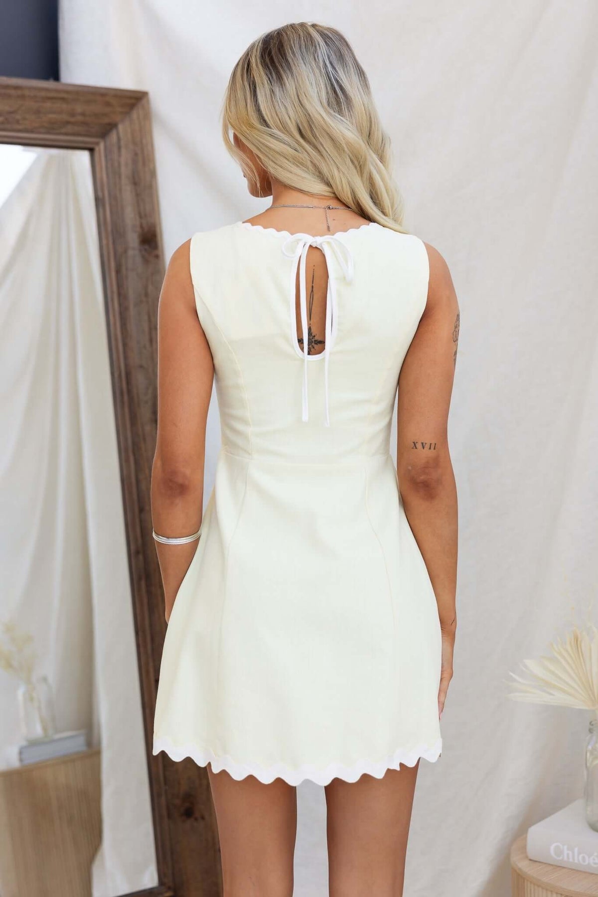 Back view of Mayfield Dress featuring a high neckline, tie back detail, and scalloped hem, perfect for summer occasions.
