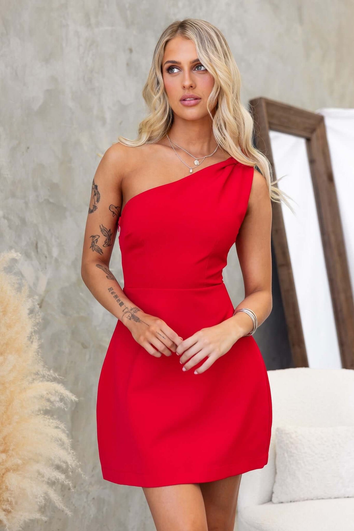 Model wearing a red one-shoulder Fallow dress with a twist strap in a stylish setting.