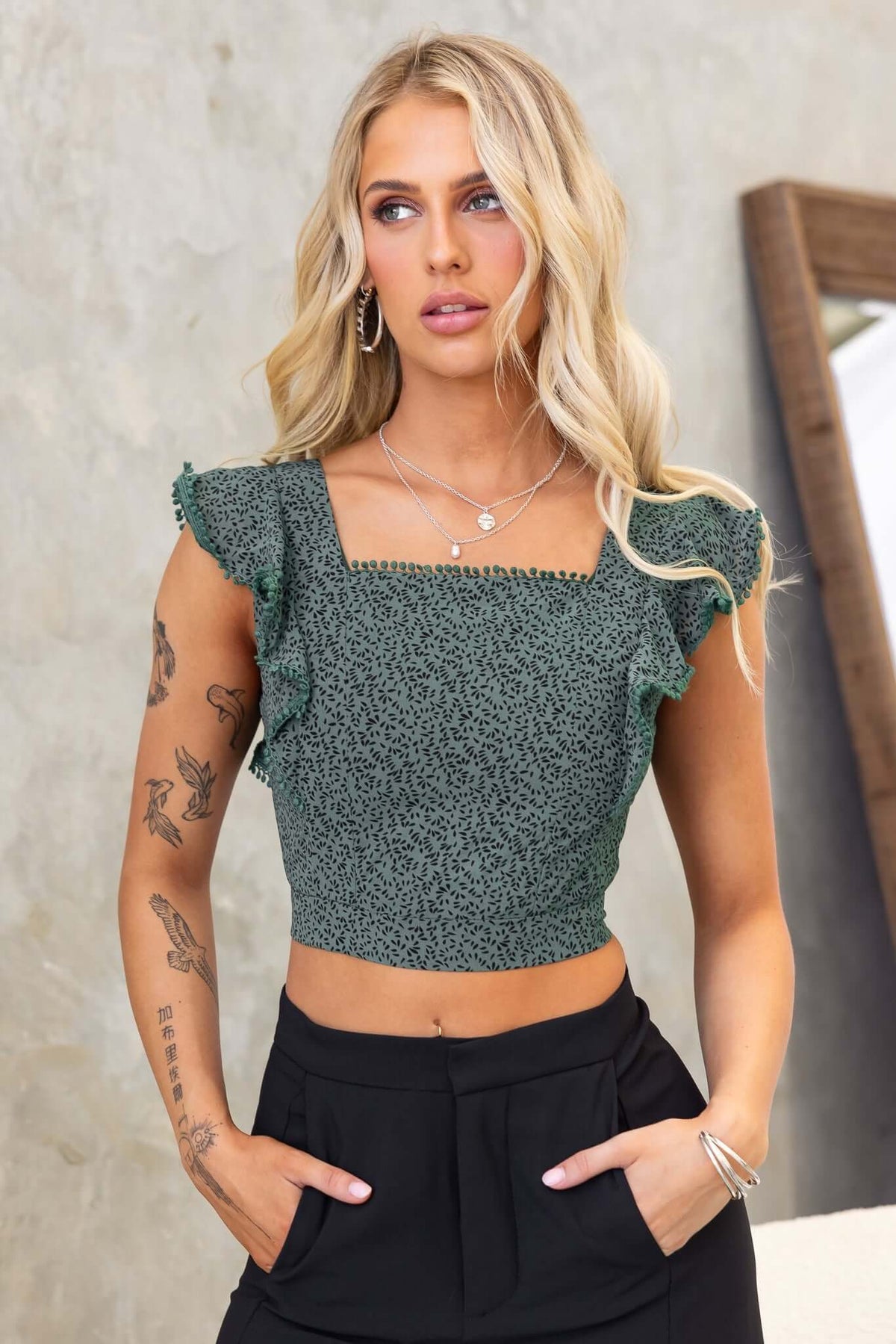 Unico Top featuring a square neckline and ruffled sleeves, styled with black trousers, ideal for casual or dressy occasions.