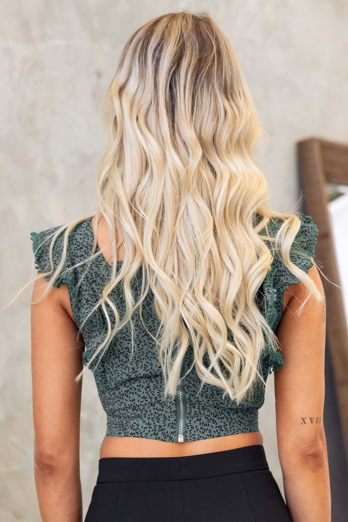 Back view of a woman in a green Unico Top with square neckline and ruffled sleeves, showcasing her long blonde hair.