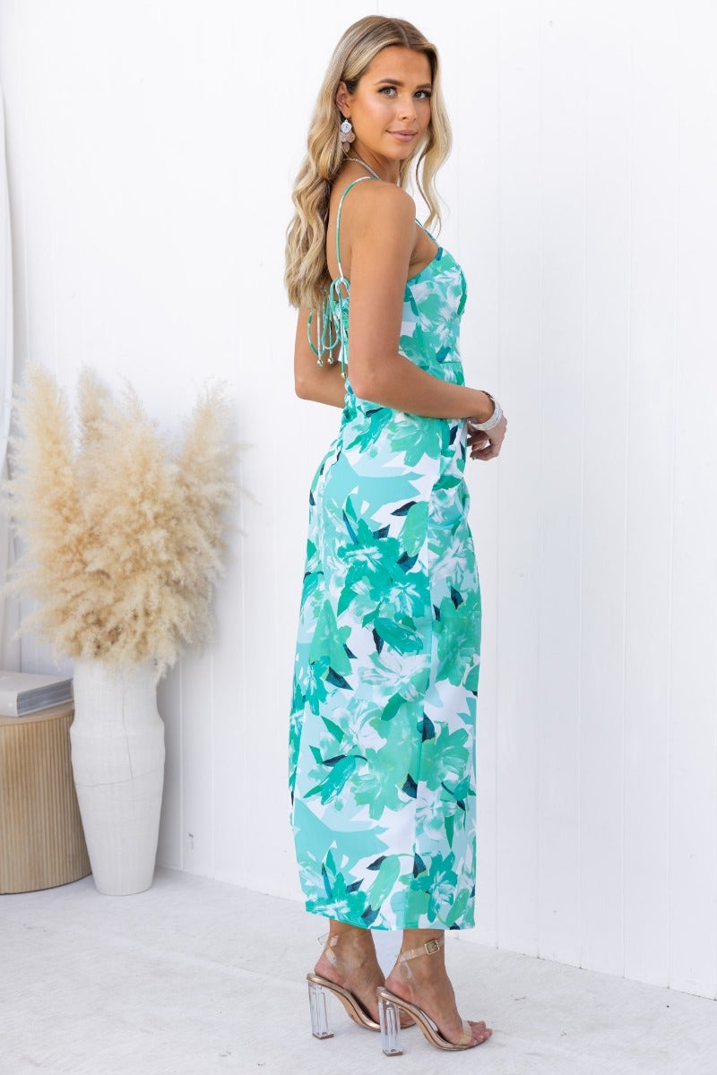 Model wearing a floral print maxi dress with adjustable straps, featuring an asymmetrical hemline and an elegant look.