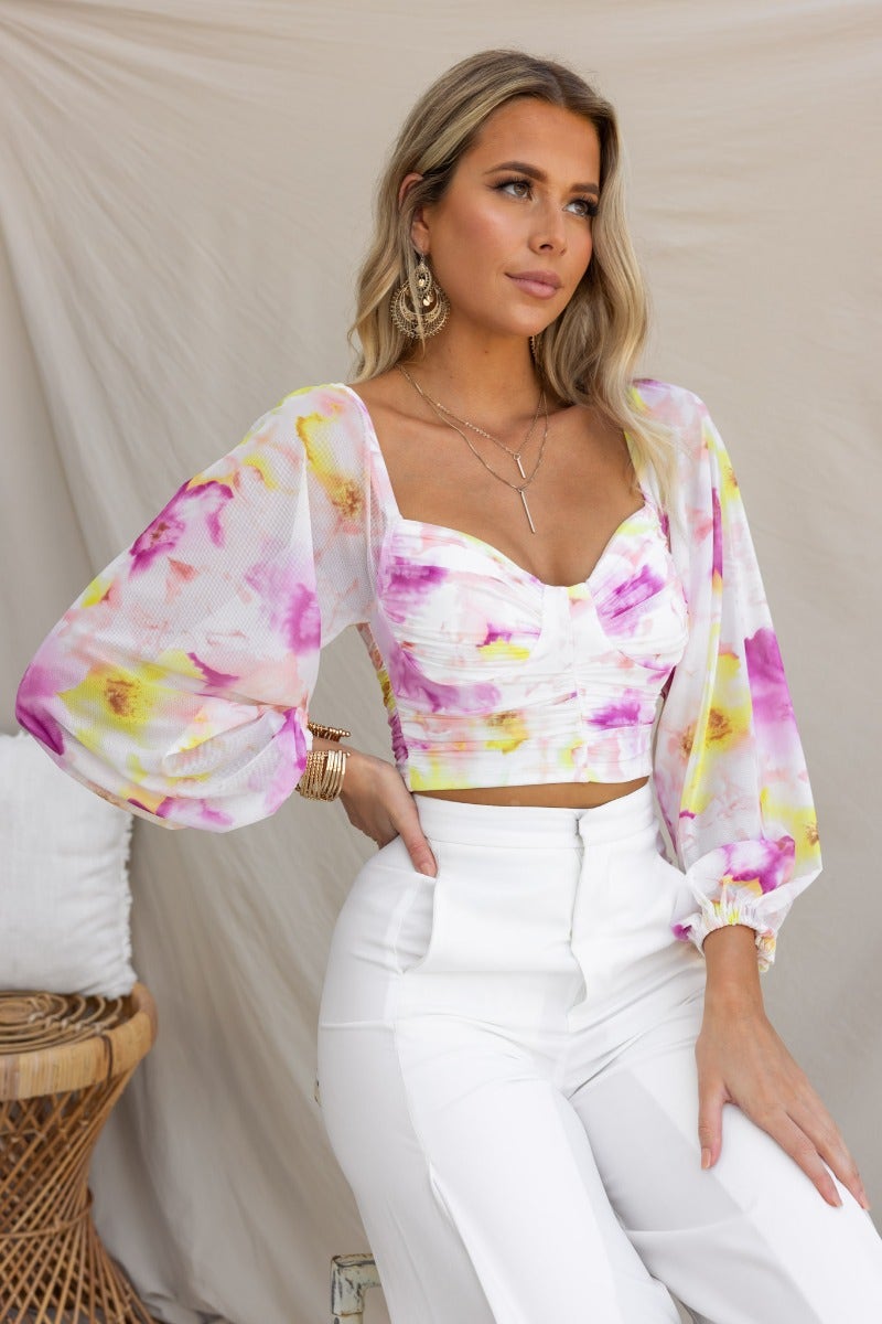 Model wearing Cate Top with mesh overlay, padded bust, and floral design, styled with white pants.