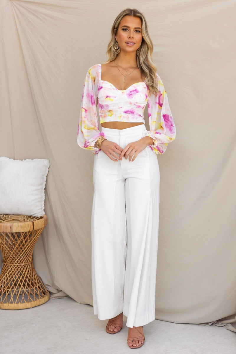 Woman wearing a floral mesh overlay Cate Top with white wide-leg pants, showcasing a stylish and elegant look.
