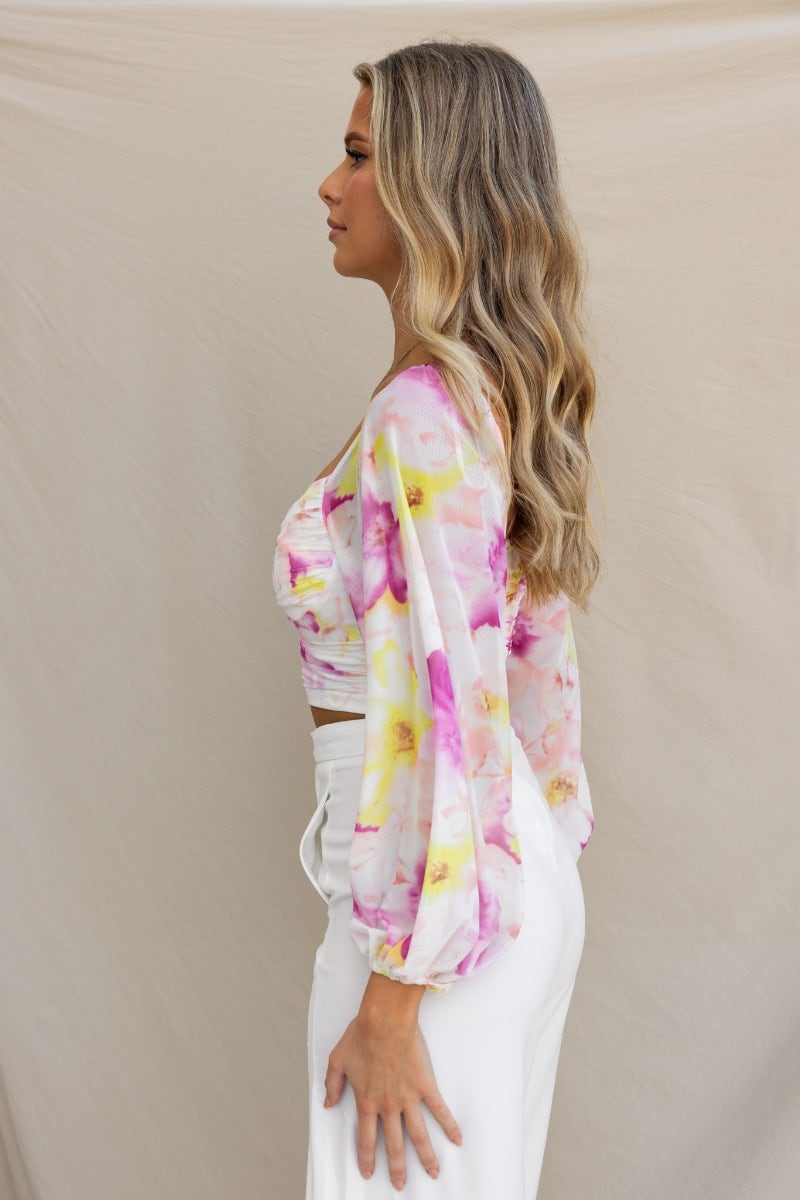 Model wearing the Cate Top, a floral mesh overlay top with elastic sleeves, showcasing a side view hairstyle and styling.