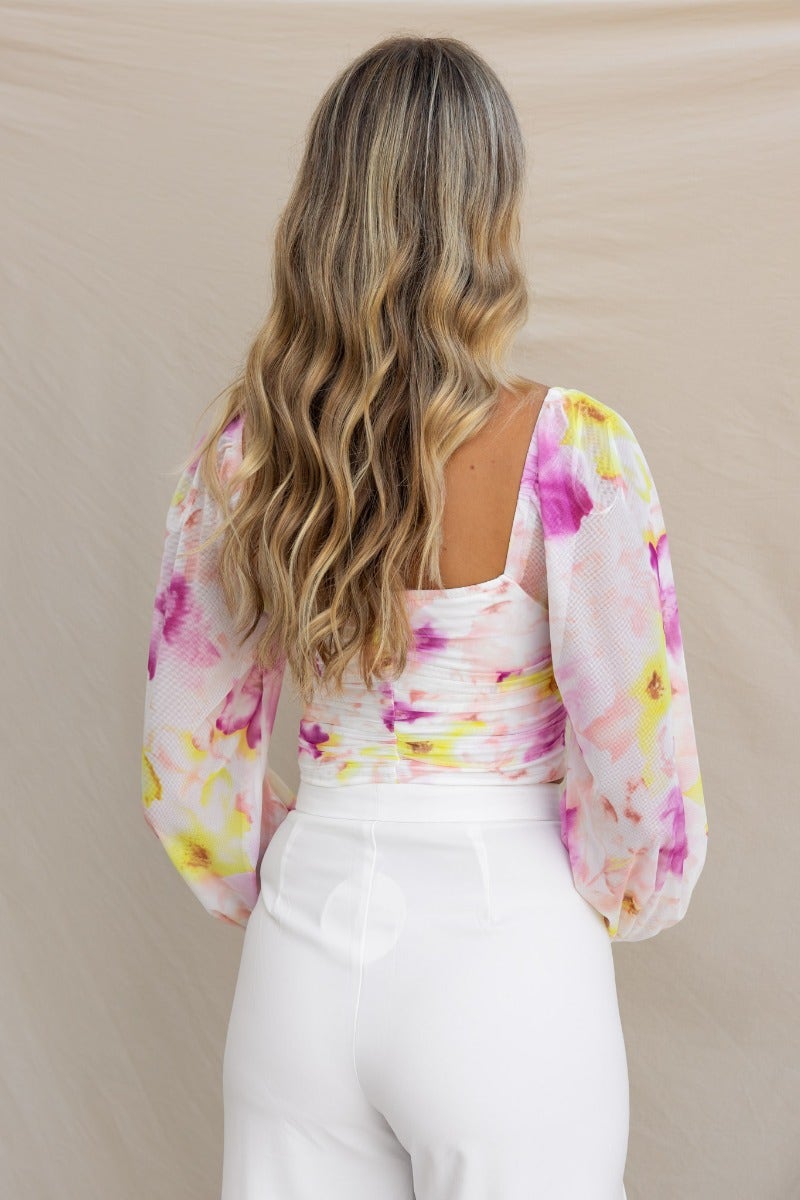 Back view of a model wearing a floral mesh overlay Cate Top with elastic sleeves and padded bust.