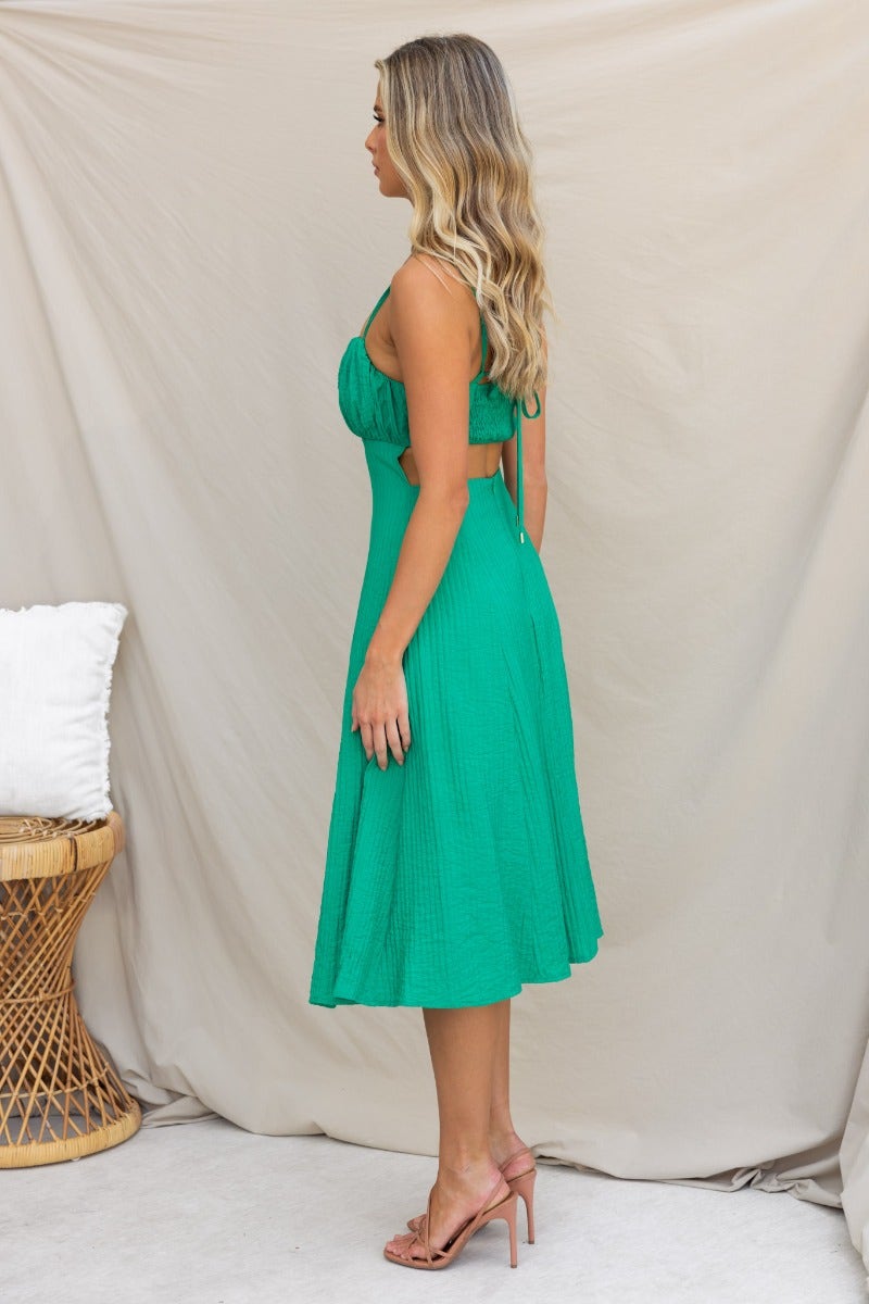 Side view of a model in a green textured midi dress with adjustable tie straps and a flowing skirt.