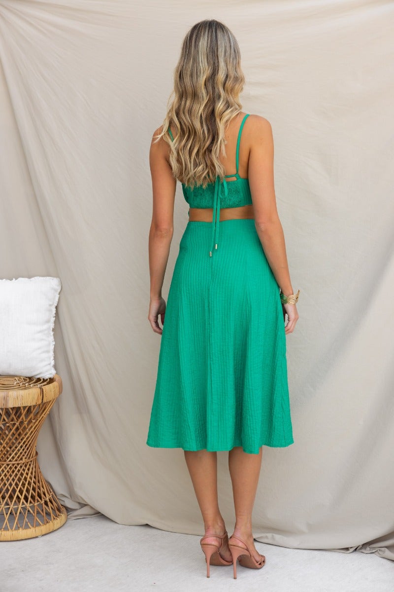 Back view of a woman in a green textured midi dress with adjustable straps and a flared skirt.