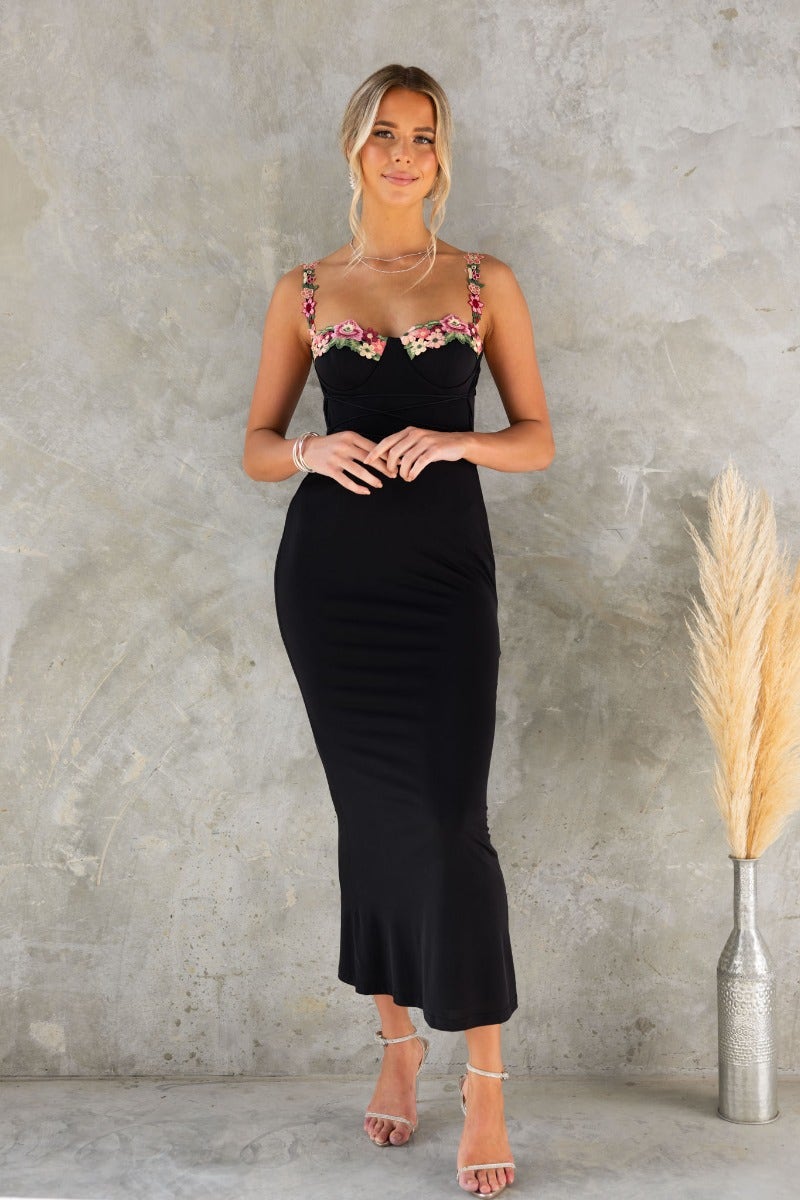 Model wearing the Eyes On Me Black Bodycon Maxi Dress with floral trim and adjustable straps.