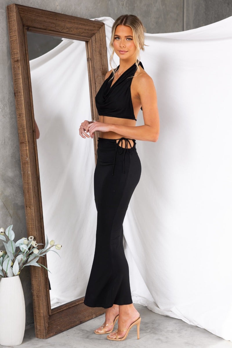 Model wearing Fearless Maxi Skirt, a black skirt with tie detail and side cut-out, styled with heels.