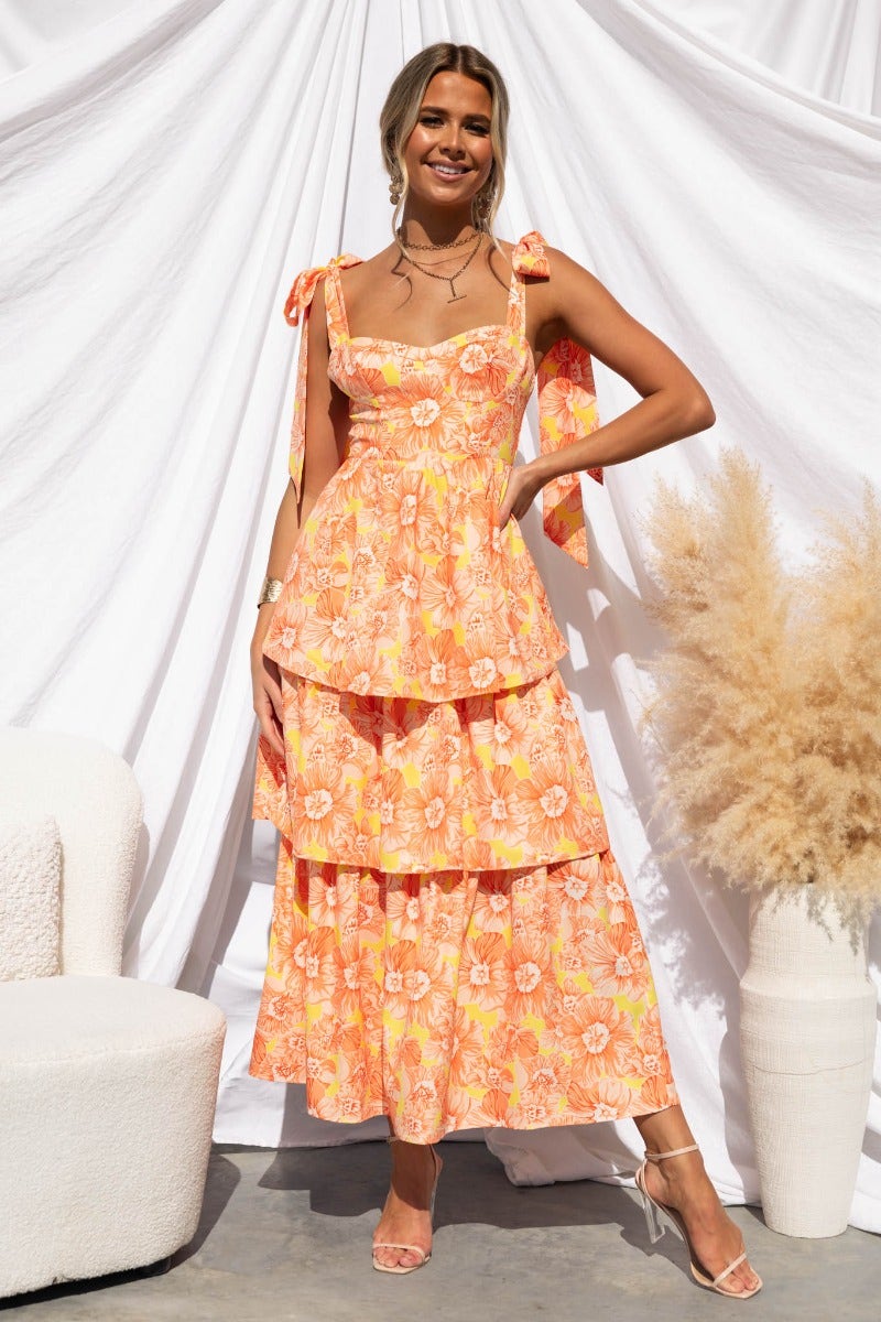 Connali Maxi Dress featuring a floral print, adjustable tie straps, and layered design, styled with a backdrop of neutral decor.